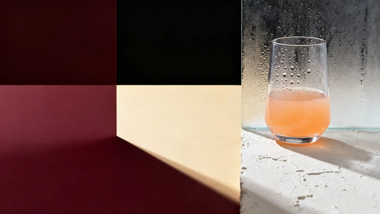 Natureza-morta em luz lateral dura: condensacao fria em gotas sobre vidro, sobre fundo vinho e creme