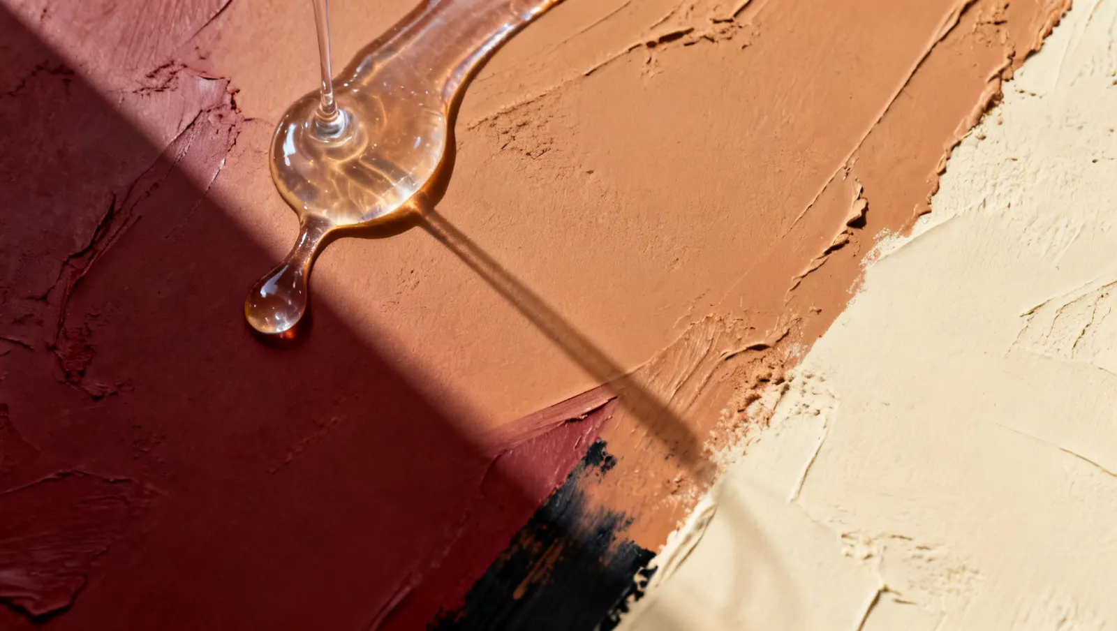 Natureza-morta em luz lateral dura: um fio de gel transparente espesso, sobre fundo vinho e creme