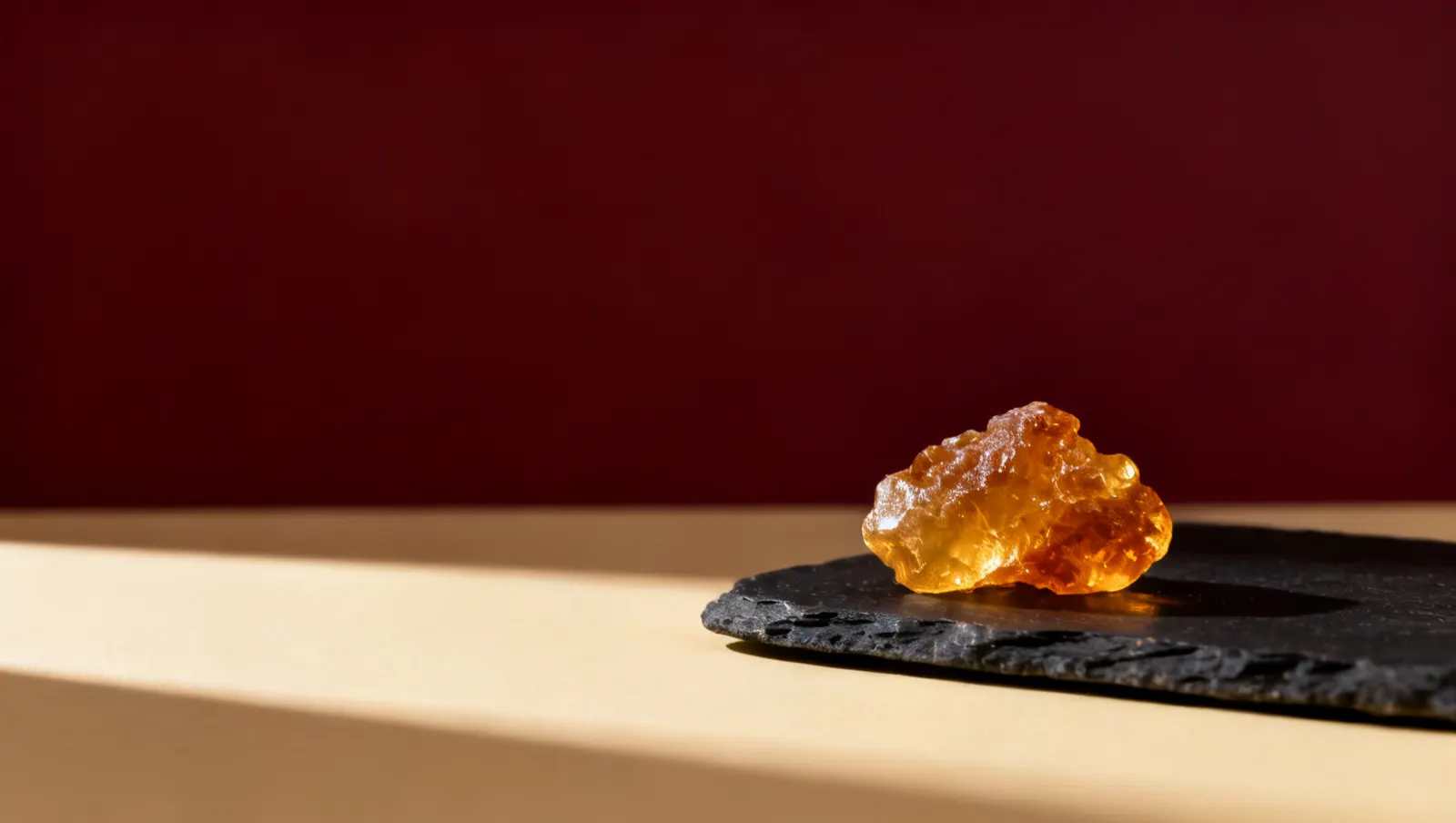 Natureza-morta em luz lateral dura: um bloco de resina de ambar dourado, sobre fundo vinho e creme